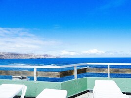 Vista al mar con barandilla y sillas reclinables blancas.
