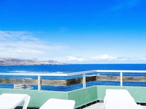 Vista al mar con barandilla y sillas reclinables blancas.