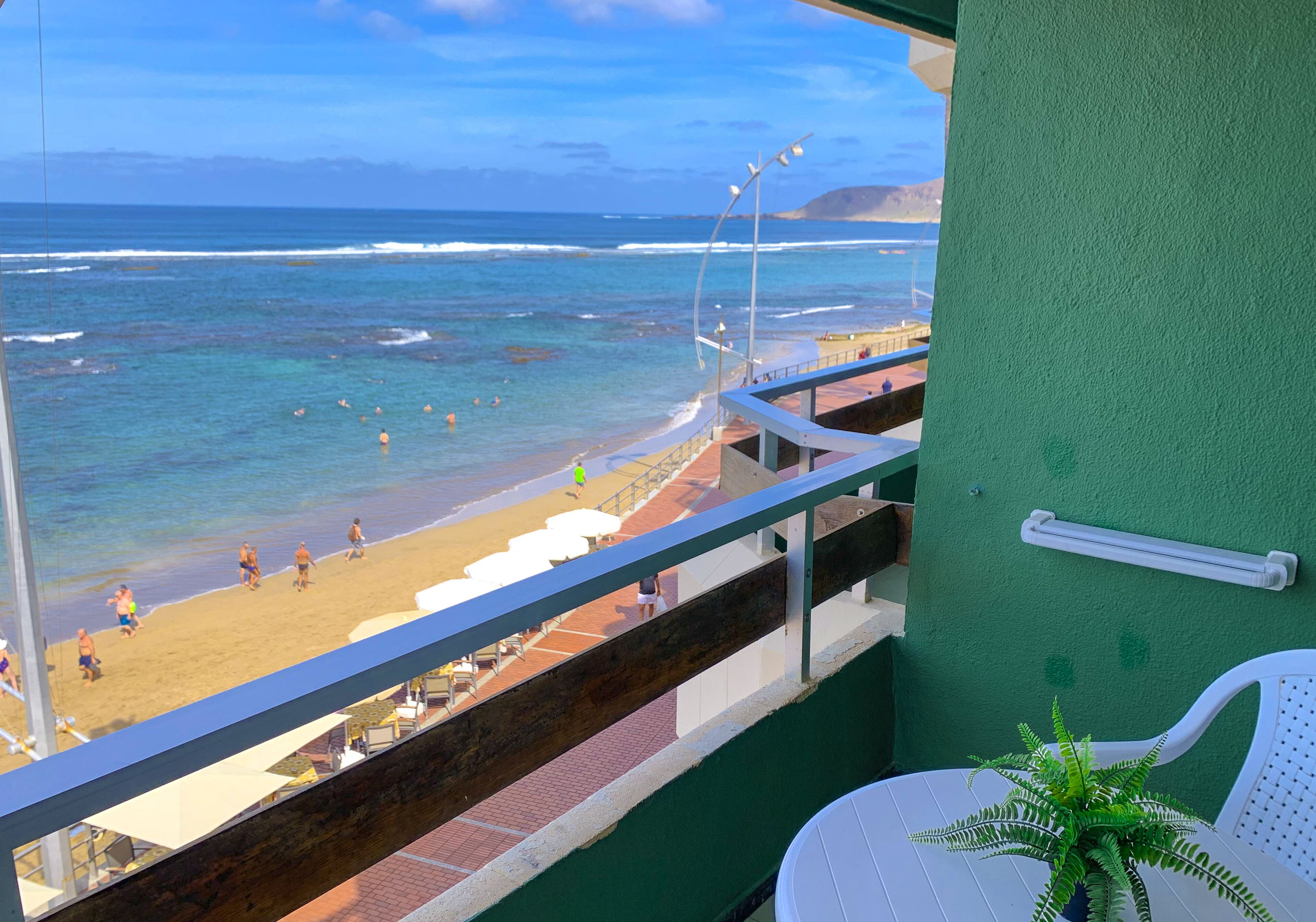 A balcony with a view of the beach, a green wall, and a potted plant.