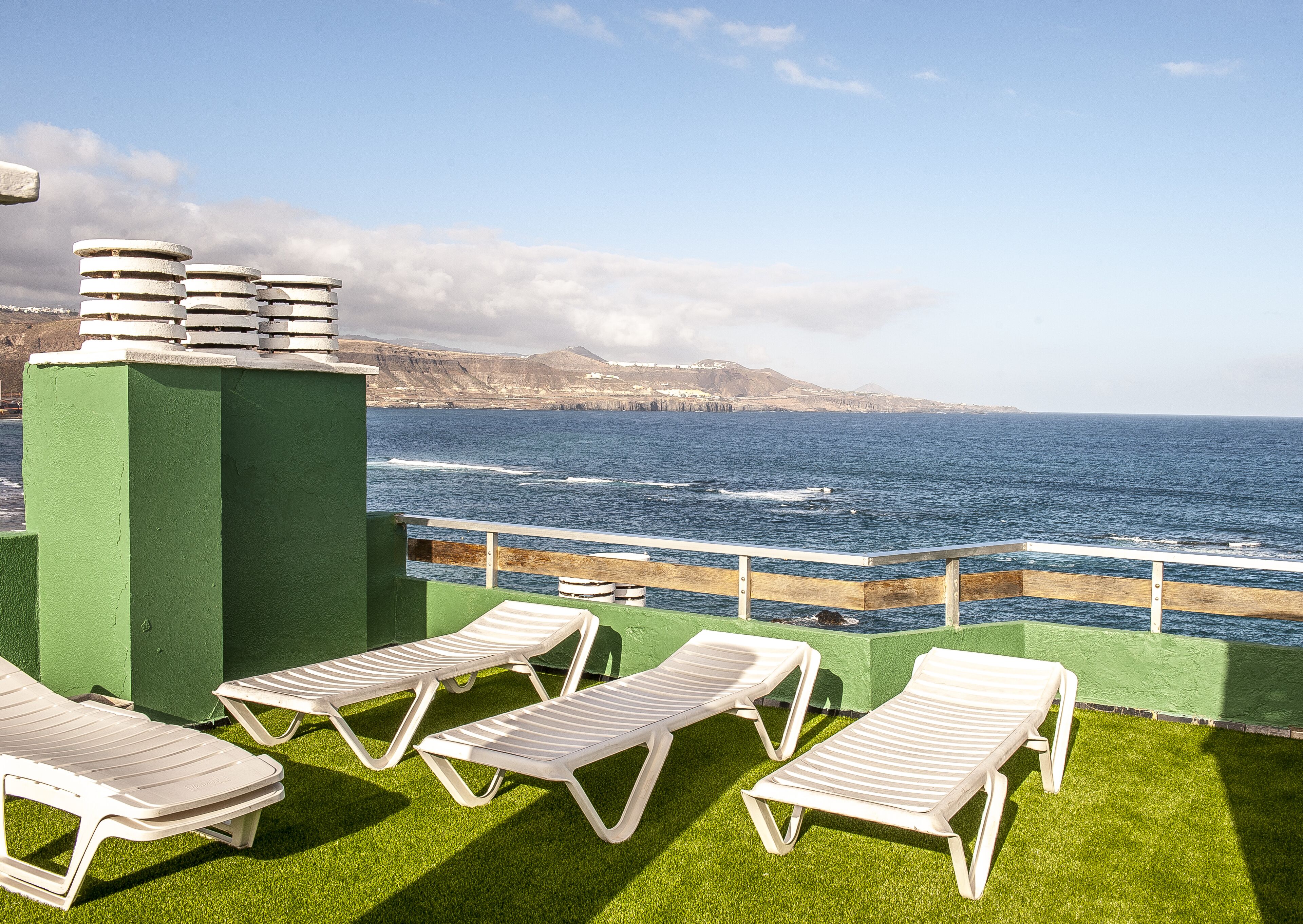 A terrace with white sun loungers and a view of the ocean.