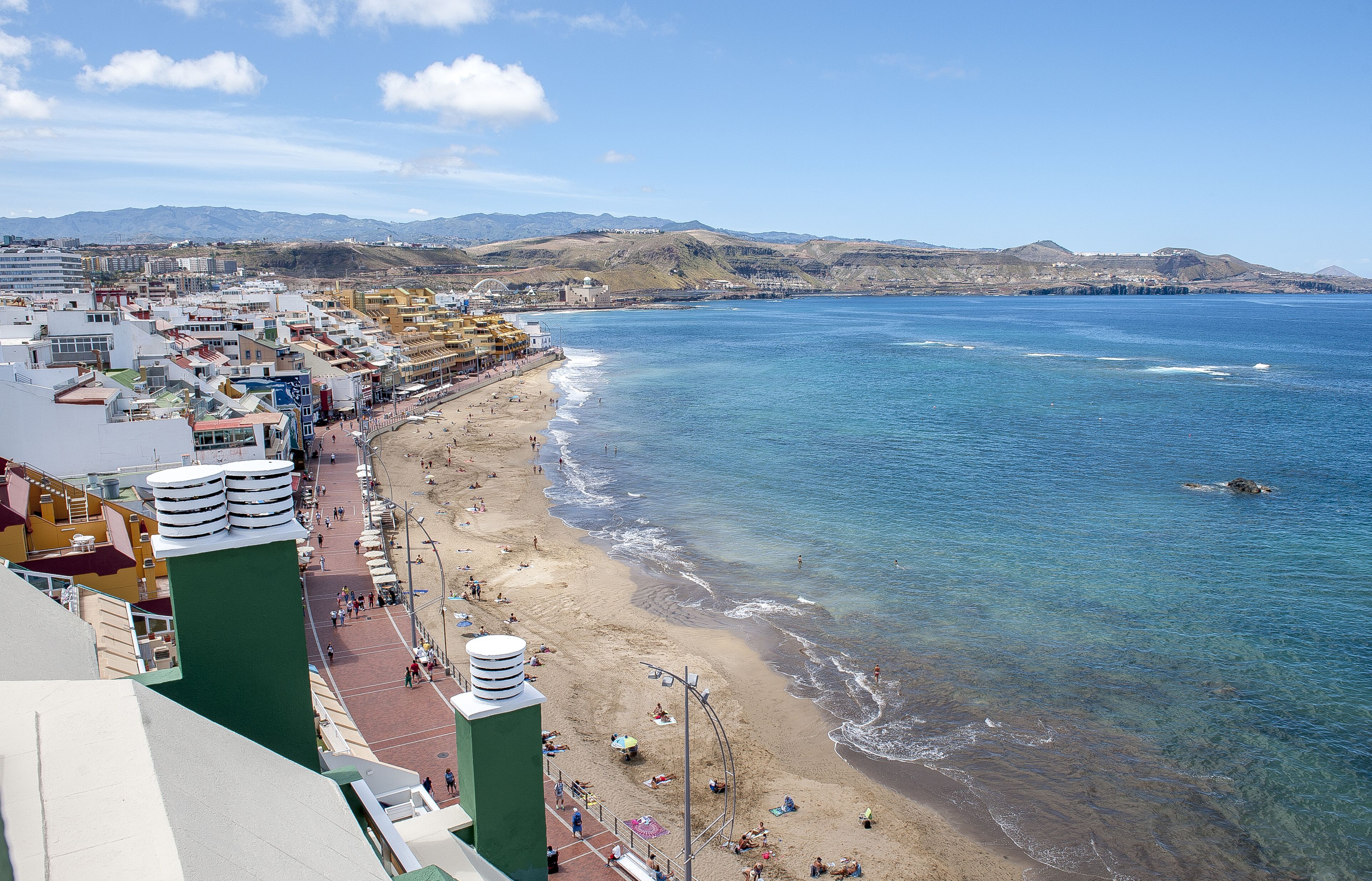 A coastal cityscape with a beach, buildings, and mountains in the background.