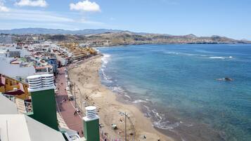 A coastal cityscape with a beach, buildings, and mountains in the background.