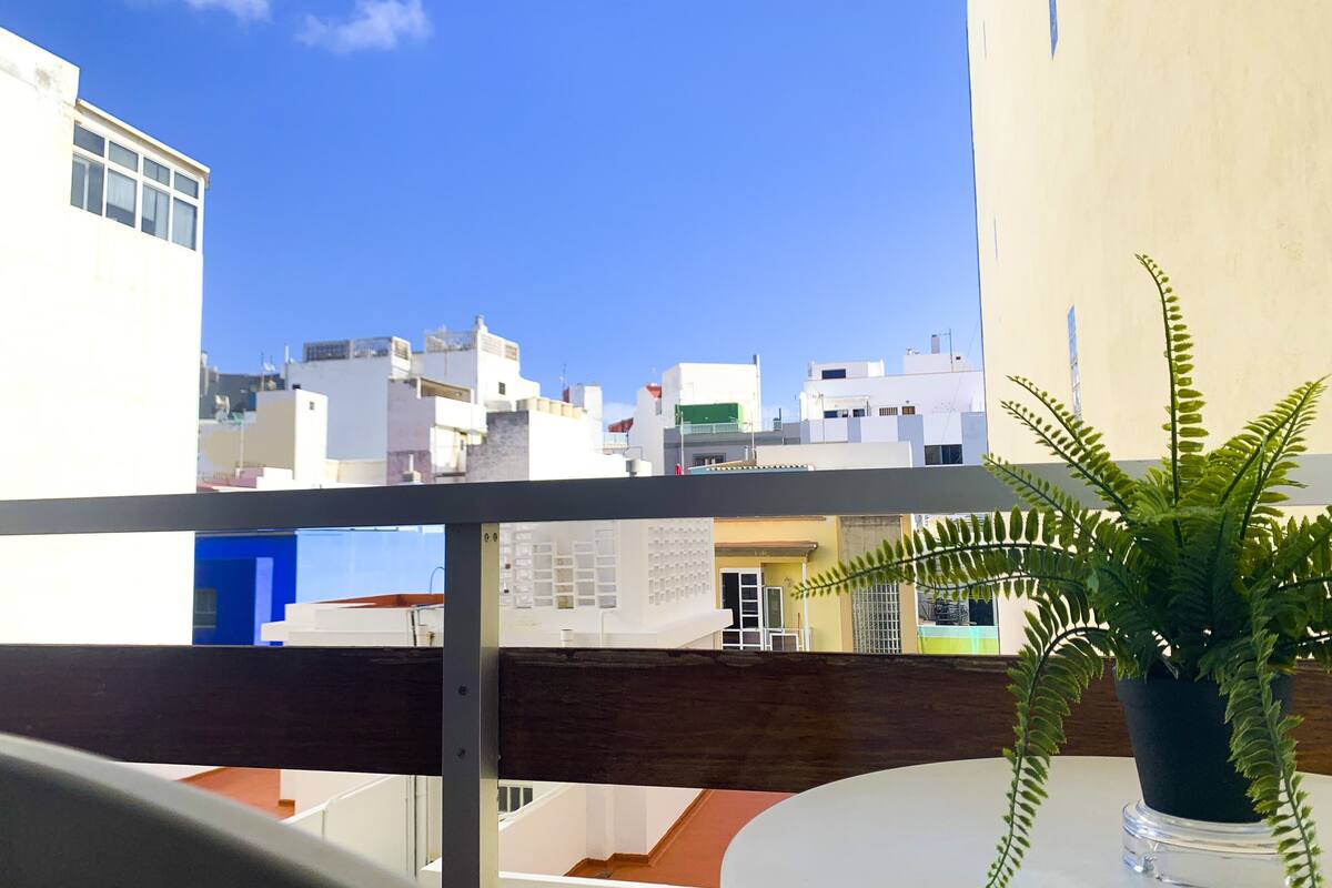 A balcony with a view of a cityscape, a potted fern, and a railing.