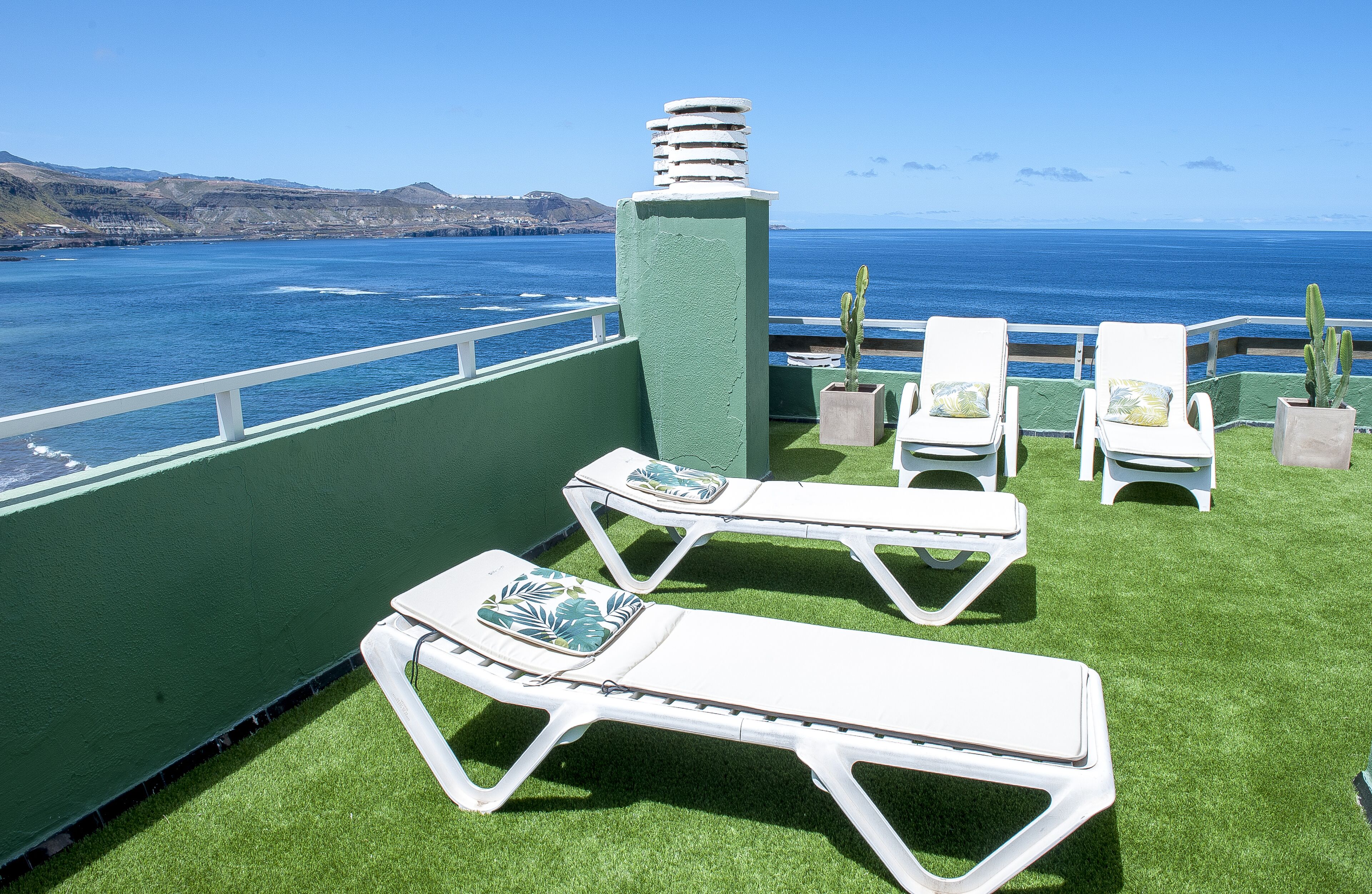Een terras met witte loungestoelen en een cactussplant, met uitzicht op een waterpartij en heuvels in de verte.
