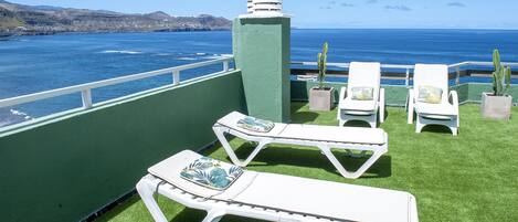 Een terras met witte loungestoelen en een cactussplant, met uitzicht op een waterpartij en heuvels in de verte.