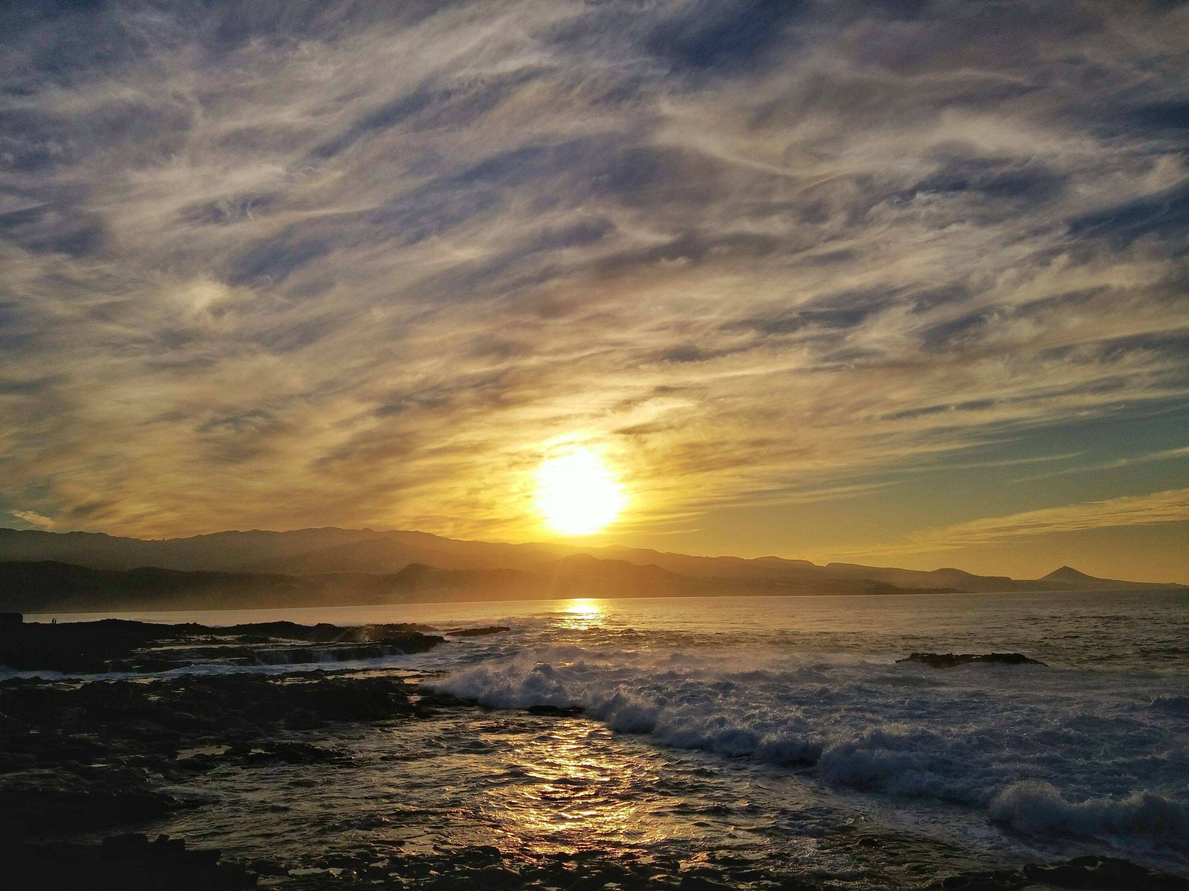 A sunset over a rocky coastline with waves crashing onto the shore.