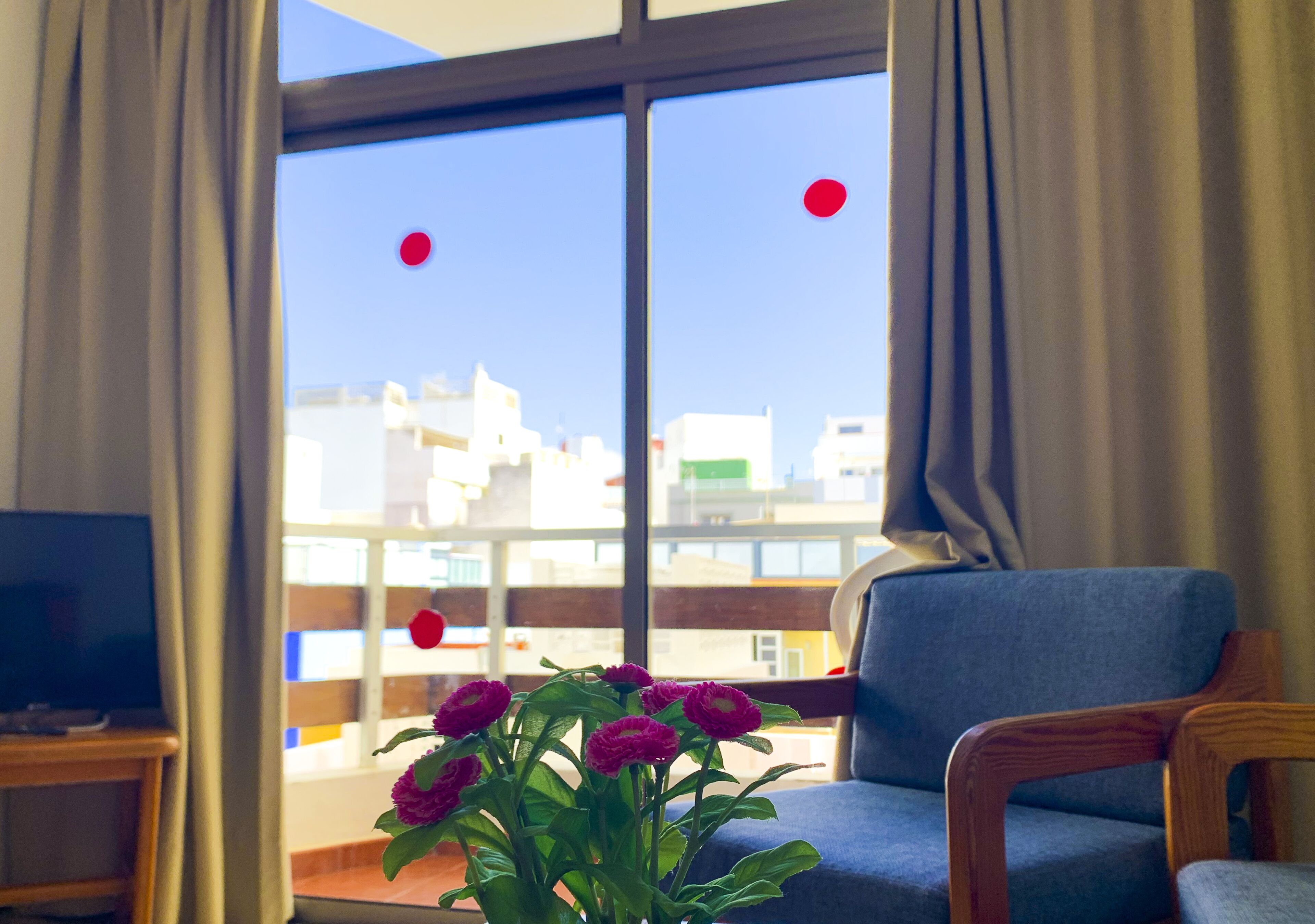 Ein Zimmer mit einem großen Fenster, einem blauen Stuhl und einem kleinen Tisch mit Blumen in einer Vase.