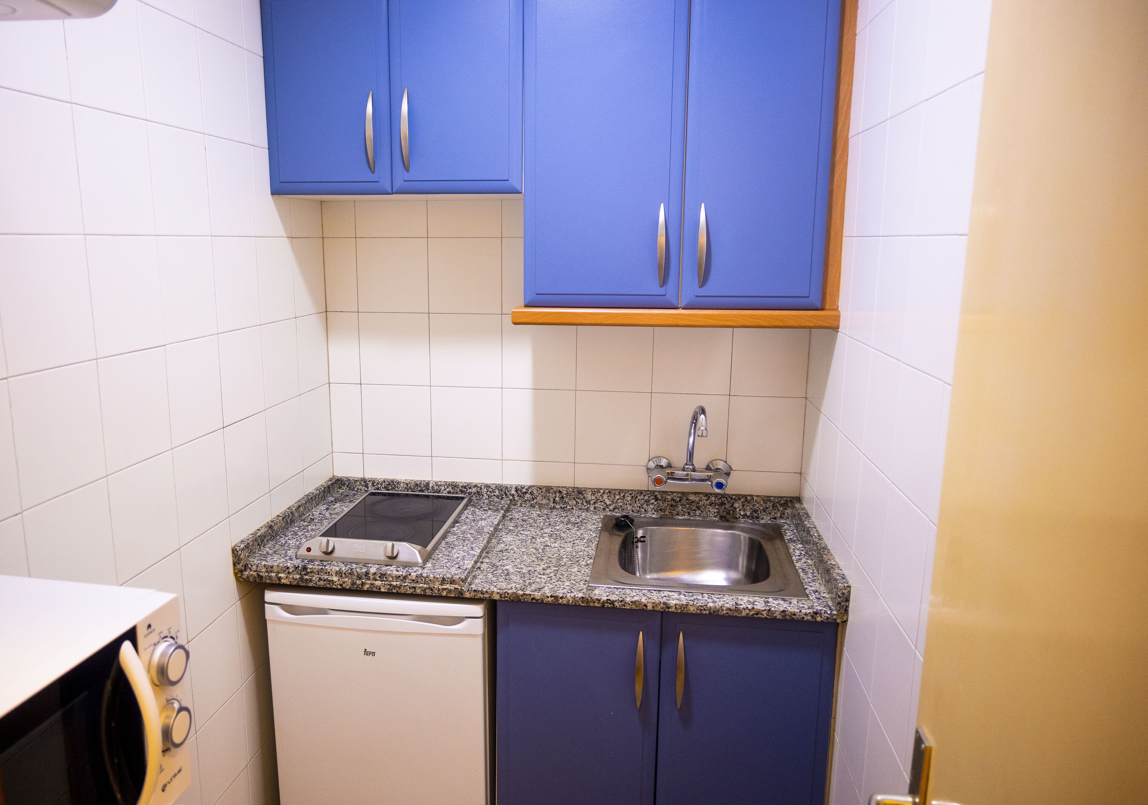 Una cocina compacta con armarios azules, una encimera de granito, un lavaplatos de acero inoxidable y un lavavajillas.