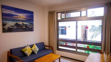 Una habitación con un sofá azul, una mesa de madera y un amplio ventanal con cortinas.