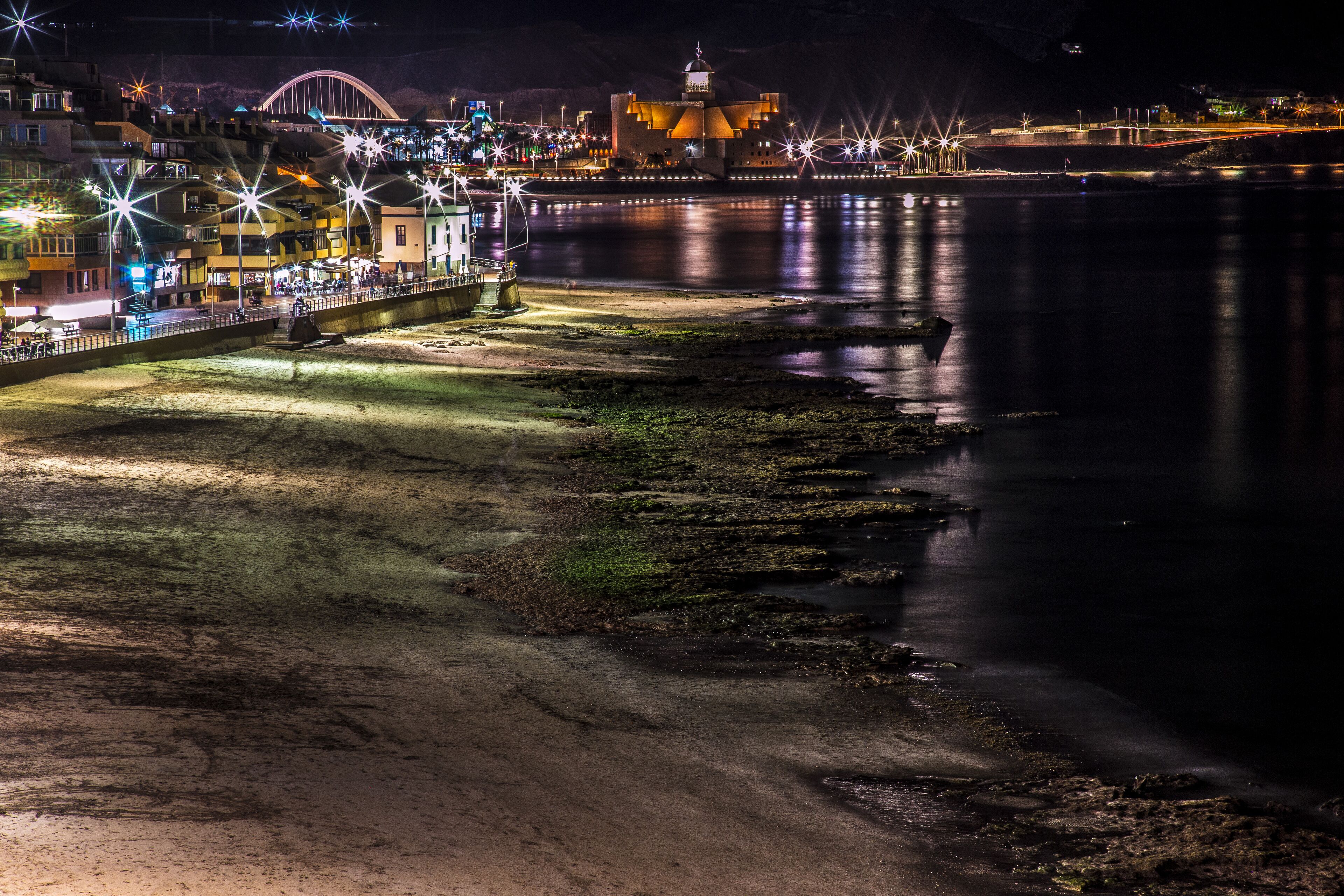 Un paseo marítimo iluminado de noche con edificios brillantes y un mar tranquilo.