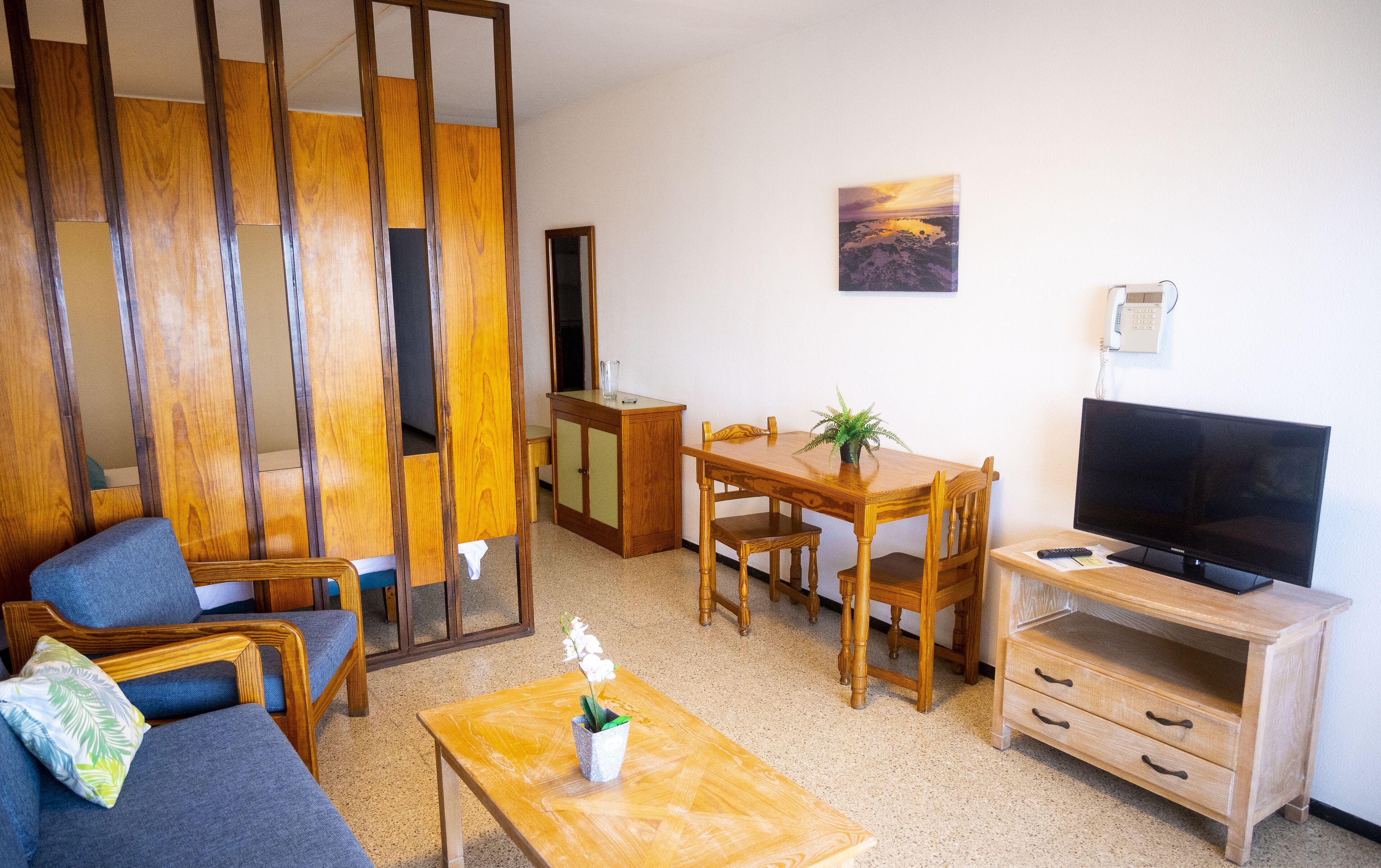 Una sala de estar con un sofá, una mesa de comedor de madera con sillas, un televisor y un mueble bajo.