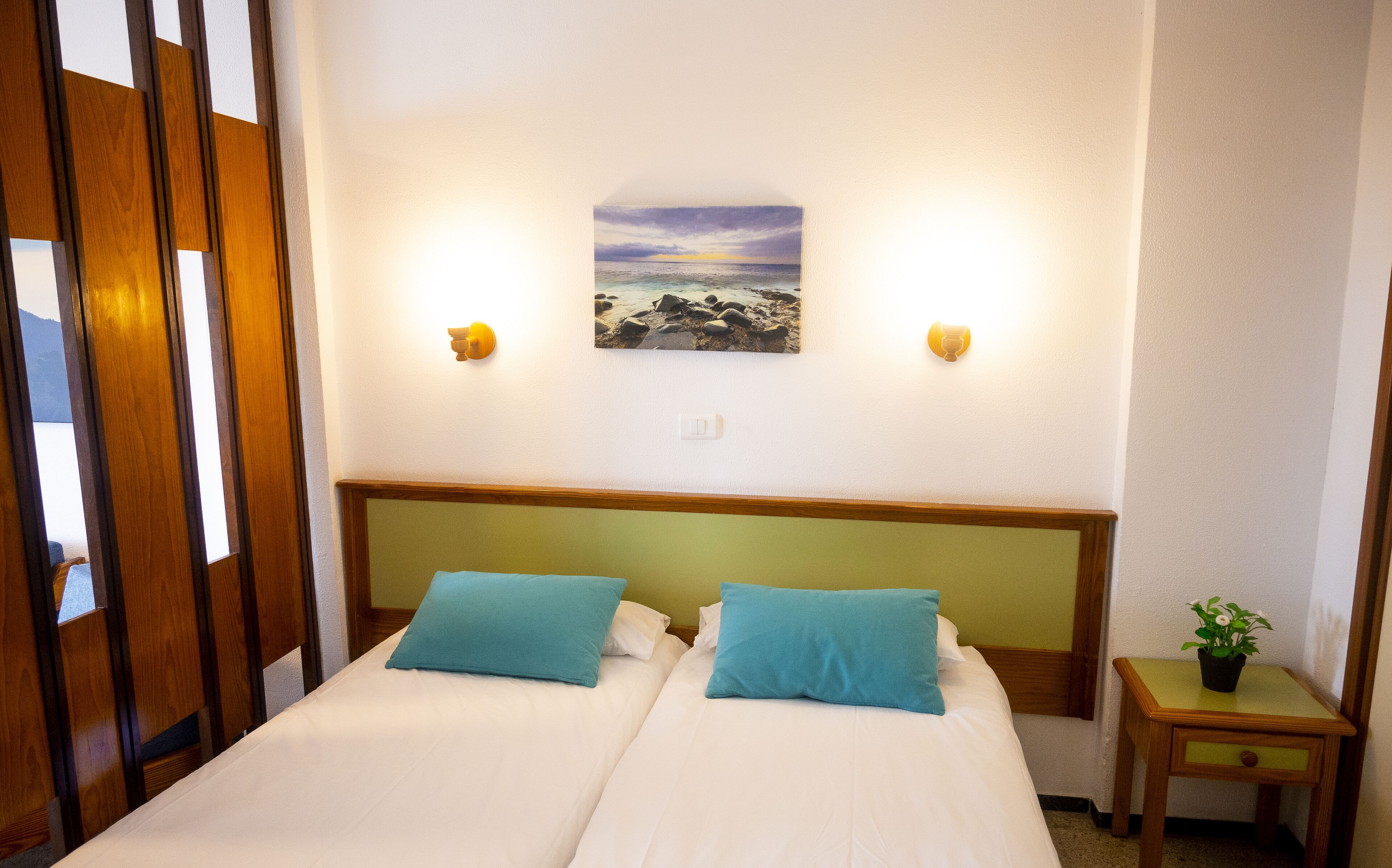 Une chambre d’hôtel avec deux lits, un tableau représentant une scène de plage et une petite table sur laquelle est posée une plante.