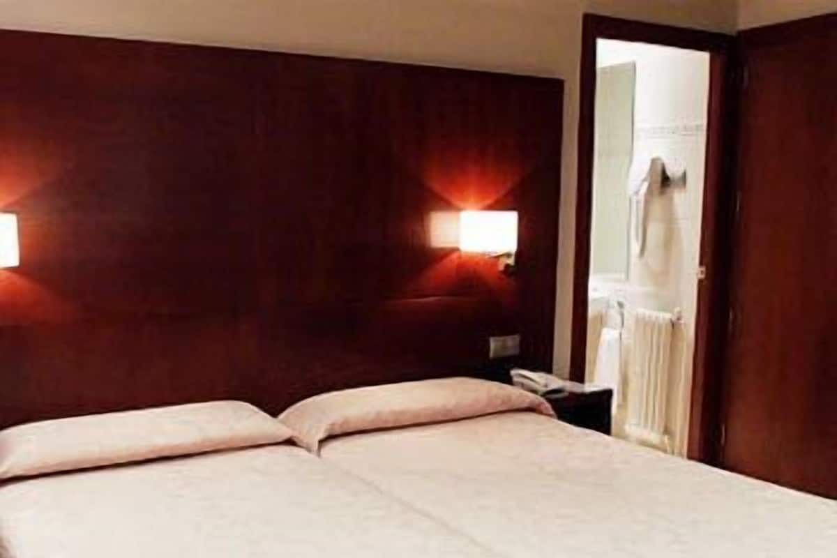 A double bed with a wooden headboard, two bedside lamps, and a nightstand with a telephone.