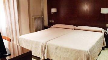 Una cama doble con cabecera de madera, dos lámparas de noche y un radiador.