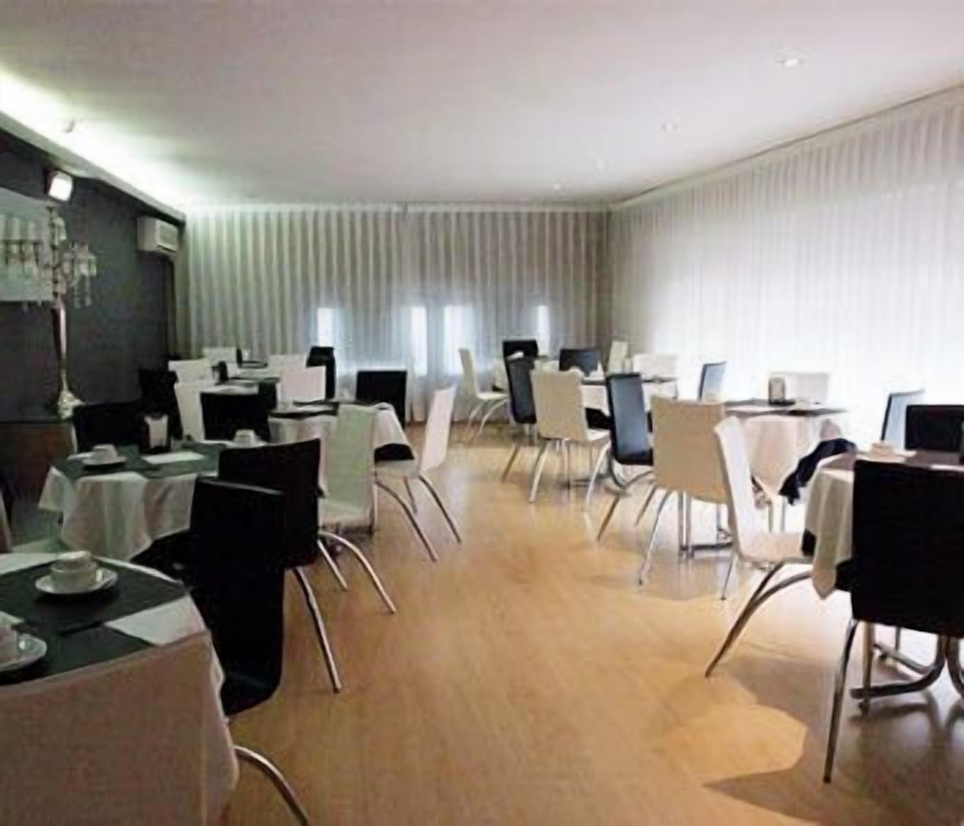 A conference room with multiple tables and chairs, large windows with blinds, and a wooden floor.