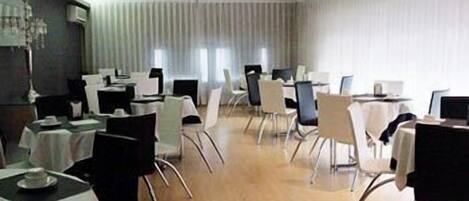 A conference room with multiple tables and chairs, large windows with blinds, and a wooden floor.