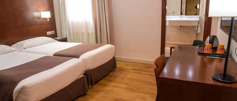 Habitación de hotel con dos camas, un escritorio de madera, un espejo y una ventana con cortinas.