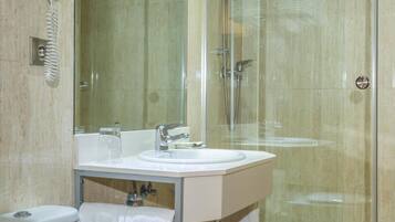 Un baño con ducha de vidrio, lavamanos blanco y retrete.