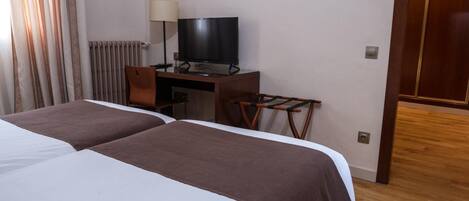 Una habitación de hotel con dos camas, un escritorio con televisor, una silla y suelo de madera.