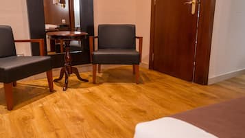 Habitación de hotel con suelo de madera, dos sillones negros, una mesita de madera y una puerta de madera.