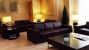 A hotel lobby with a dark leather sofa, a glass coffee table, and two lamps on side tables. - Ramón Berenguer IV (Lleida)