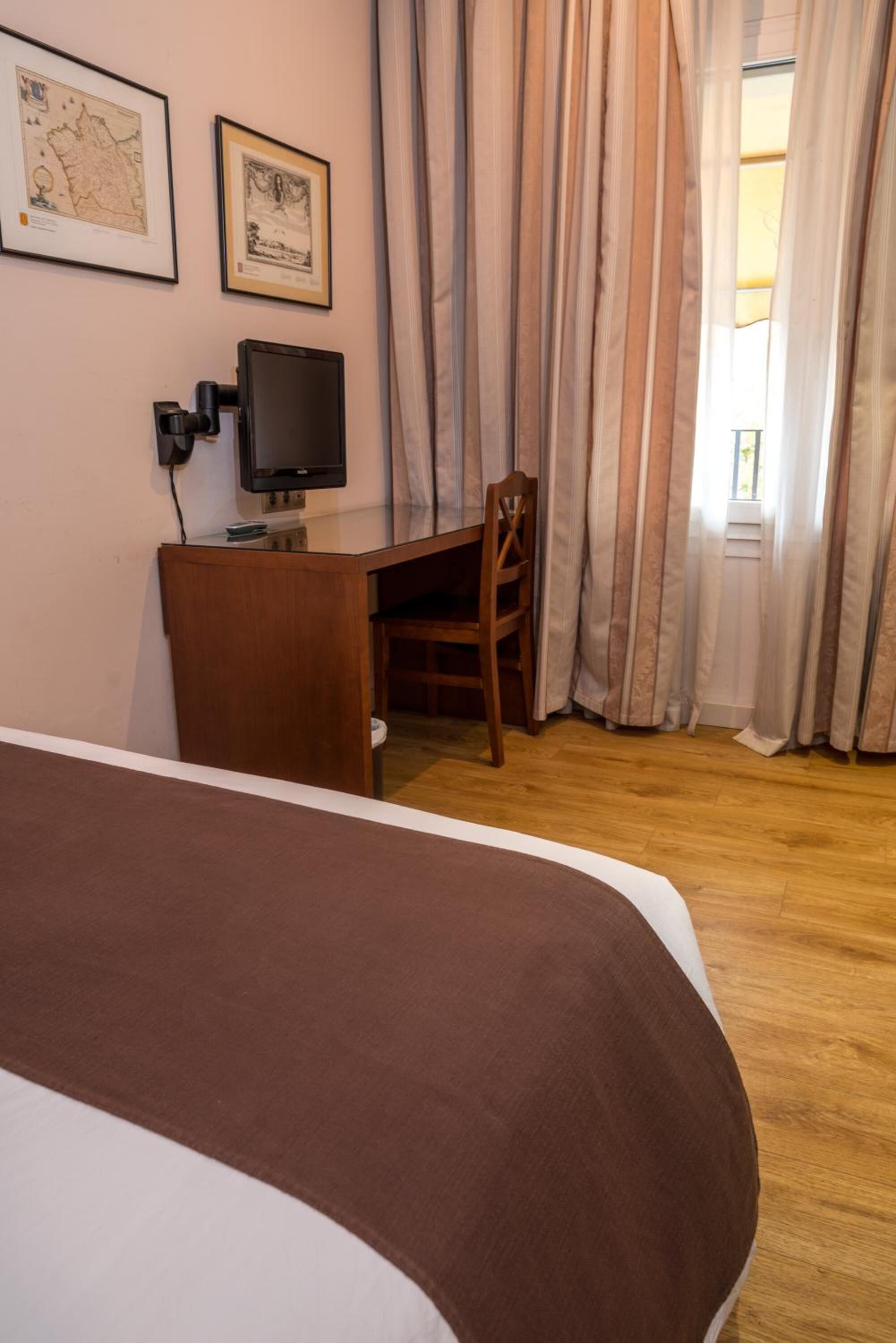 A hotel room with a bed, a desk, a chair, and curtains.