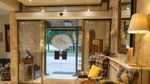 A lobby with a checkered sofa, a lamp, and a glass door entrance. - Ramón Berenguer IV (Lleida)