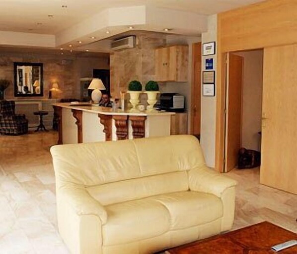 A living room with a beige sofa, a wooden coffee table, and a kitchen area with a counter and cabinets.
