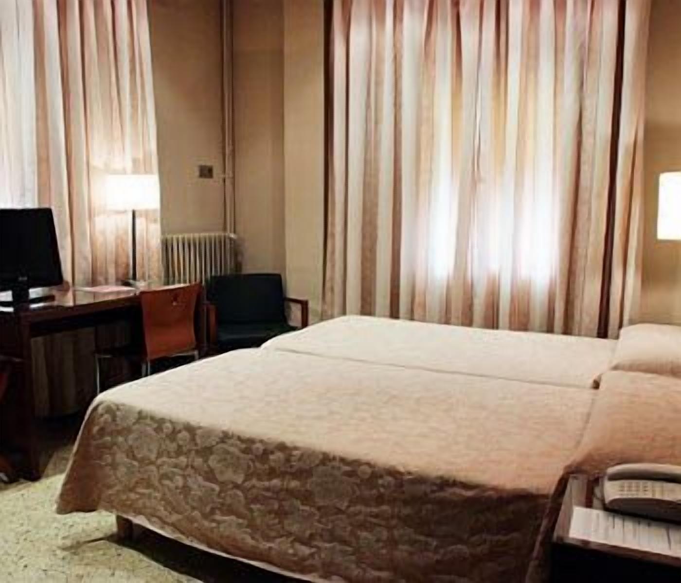 Een hotelkamer met een bed, een bureau, een stoel en een lamp.