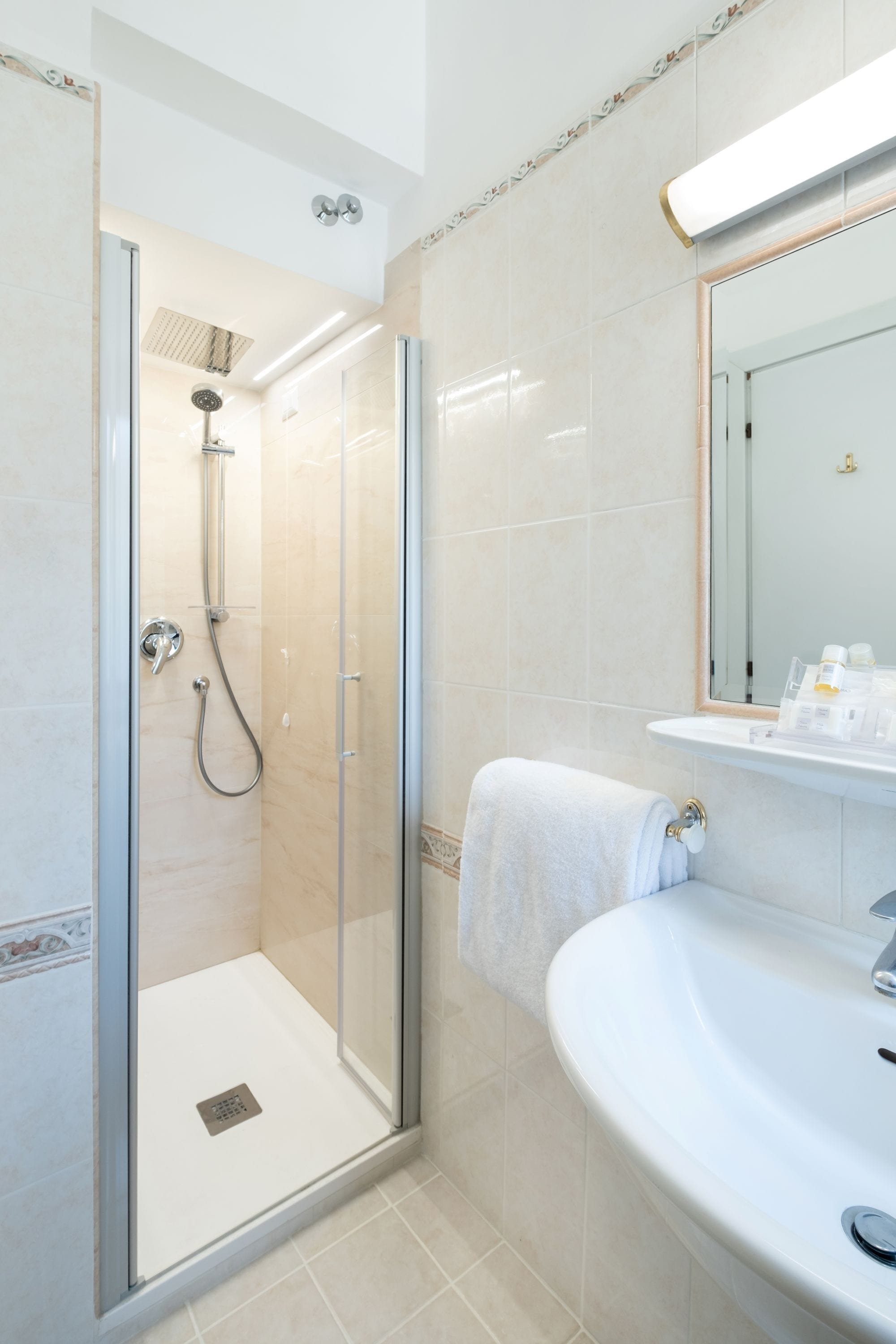 Un baño moderno con ducha de vidrio, un lavamanos blanco y un espejo sobre el lavamanos.