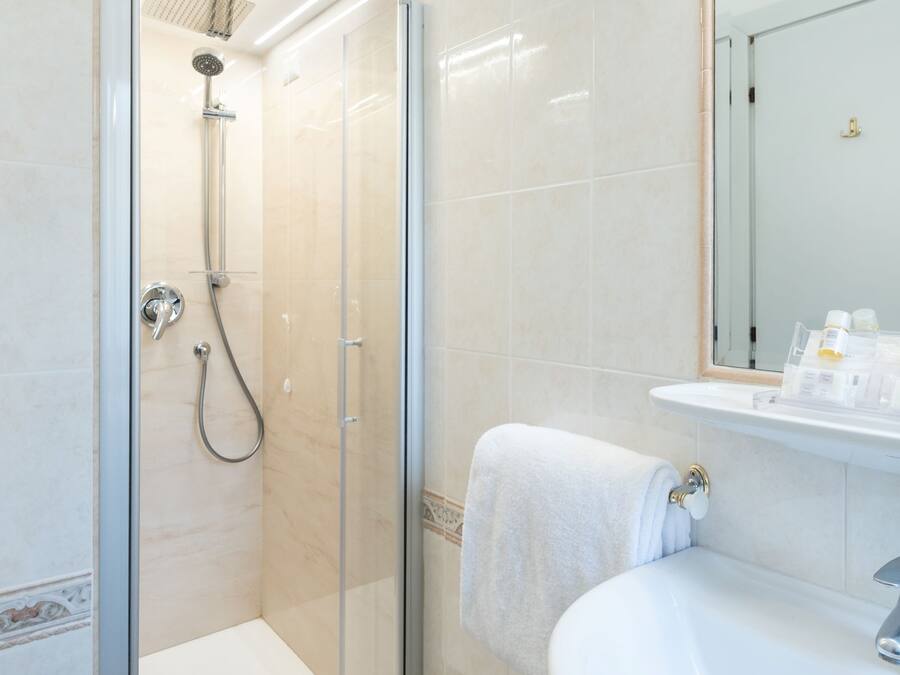 Un baño moderno con ducha de vidrio, un lavamanos blanco y un espejo sobre el lavamanos.