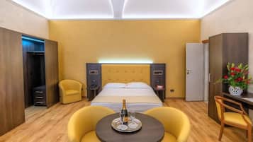 A hotel room with a bed, a bedside table with a bottle and glasses, a chair, a small table with a tray, and a wardrobe.