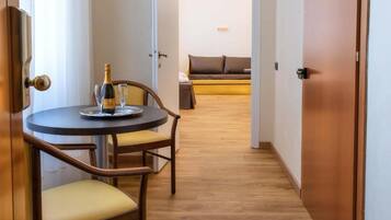 Ein Hotelzimmer mit Holzboden, einem runden Tisch mit zwei Stühlen, einer Champagnerflasche und einer Couch im Hintergrund.