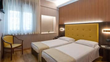 Ein Hotelzimmer mit zwei Betten, einem Sessel, einem Schreibtisch und einem Fenster mit Vorhängen.