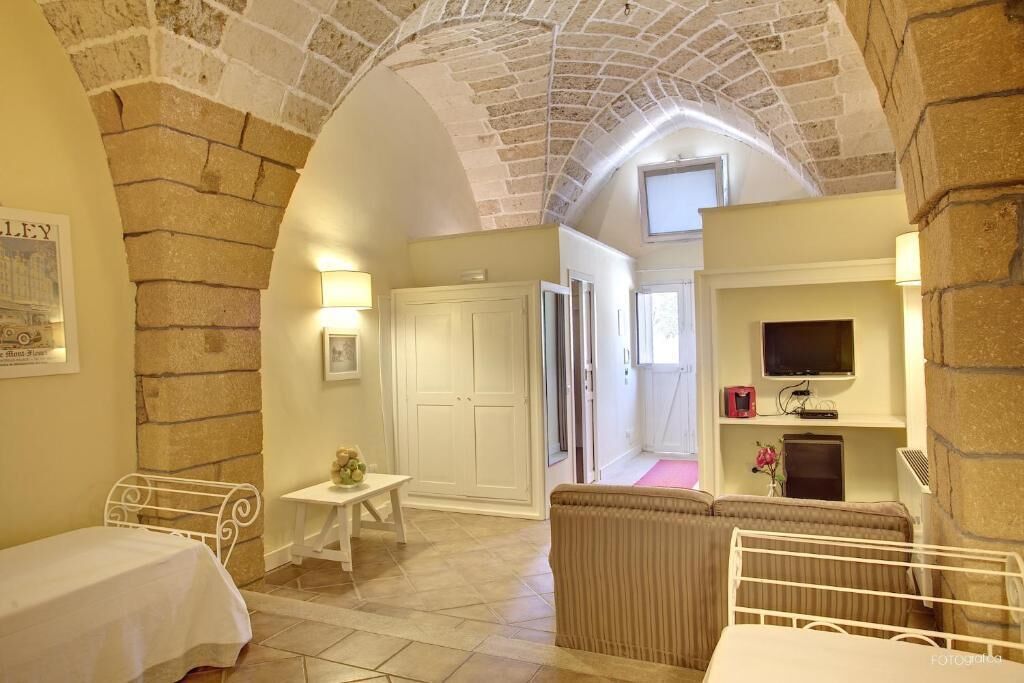 Une pièce chaleureuse avec un plafond voûté, un lit blanc, une petite table, un canapé et un téléviseur posé sur une étagère.
