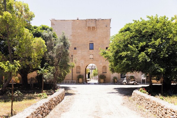 A stone building with a central archway, surrounded by trees and a gravel path.