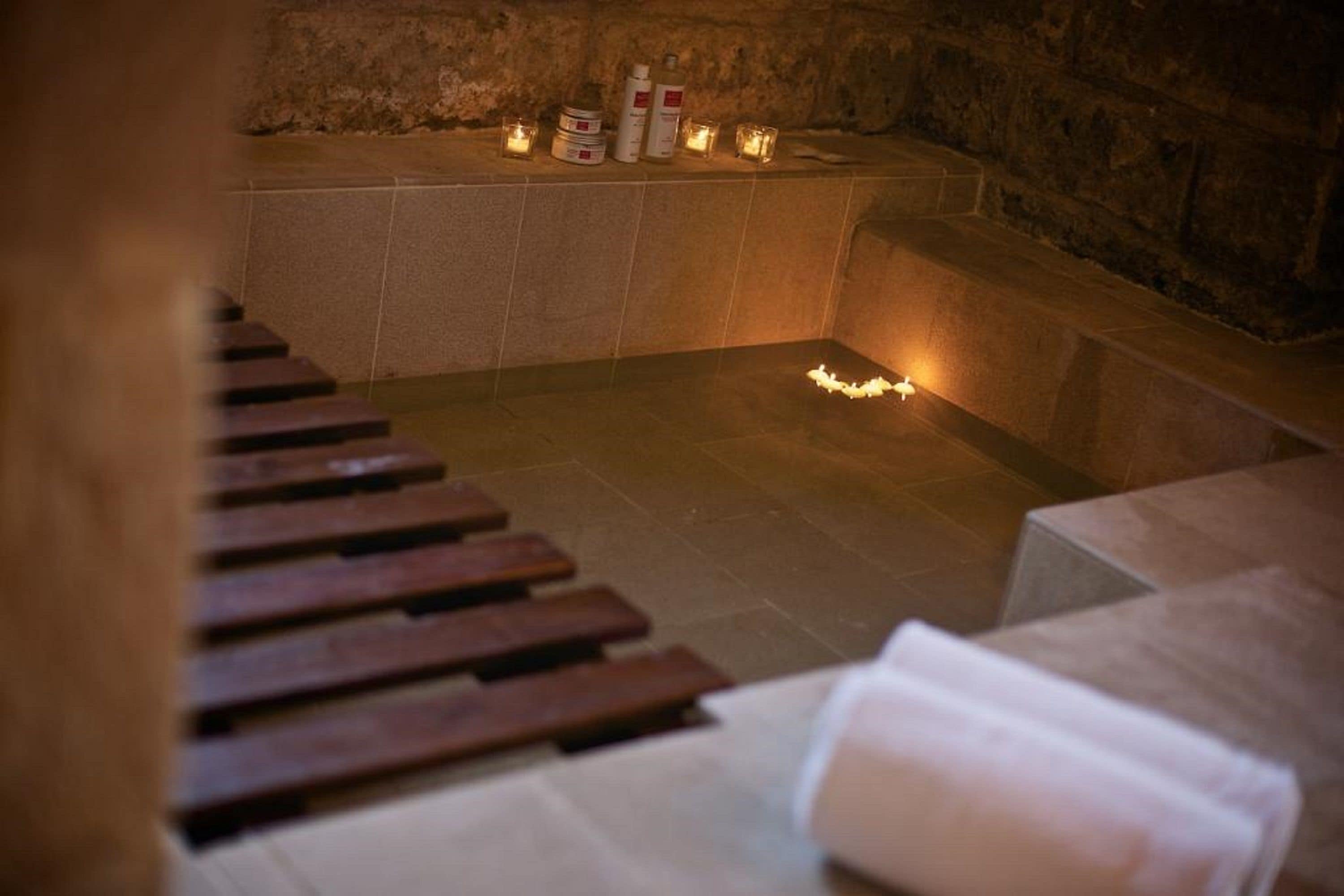 Una stanza con pareti in pietra, una panca e candele.