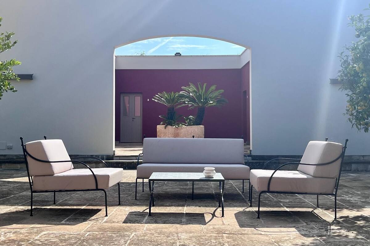 An outdoor seating area with a sofa and two chairs, a small table, and potted plants.