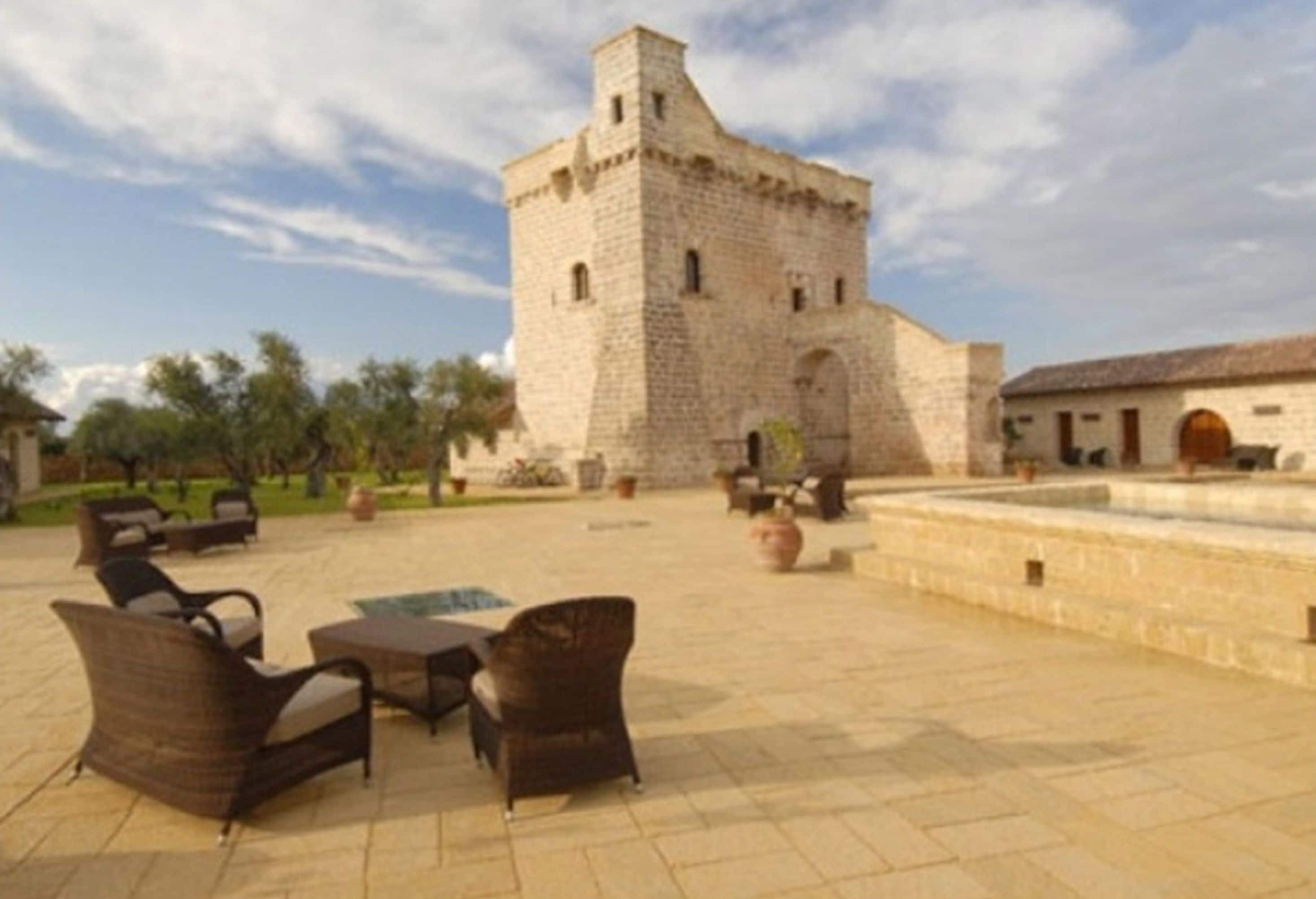 Un patio con una torre de piedra, mobiliario exterior y una fuente.