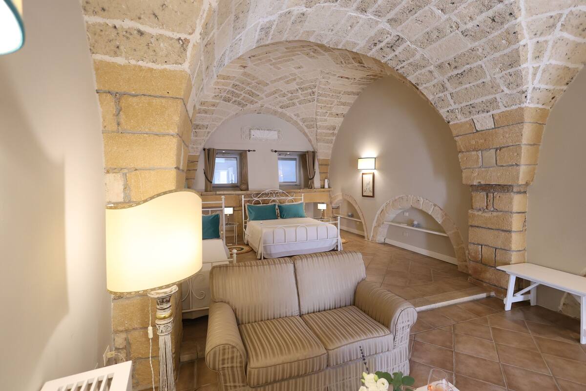 A cozy room with a stone ceiling, a sofa, a bed, and a small table.