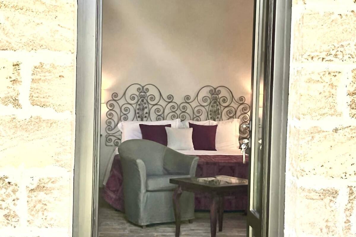 A bedroom with a metal headboard, a bed with multiple pillows, a green chair, and a small table.