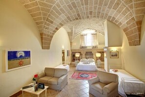 A spacious room with a high arched ceiling, a bed, two sofas, a small table, and a painting on the wall.