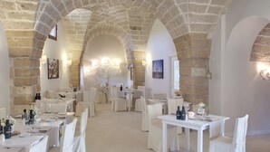 A restaurant with stone arches, white tables, and chairs, and a chandelier in the center. - Tenuta Monacelli Lecce (Lecce)