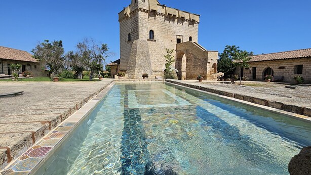 A clear pool with a stone border, a stone building with a tower, and a clear blue sky. - Tenuta Monacelli Lecce (Lecce)