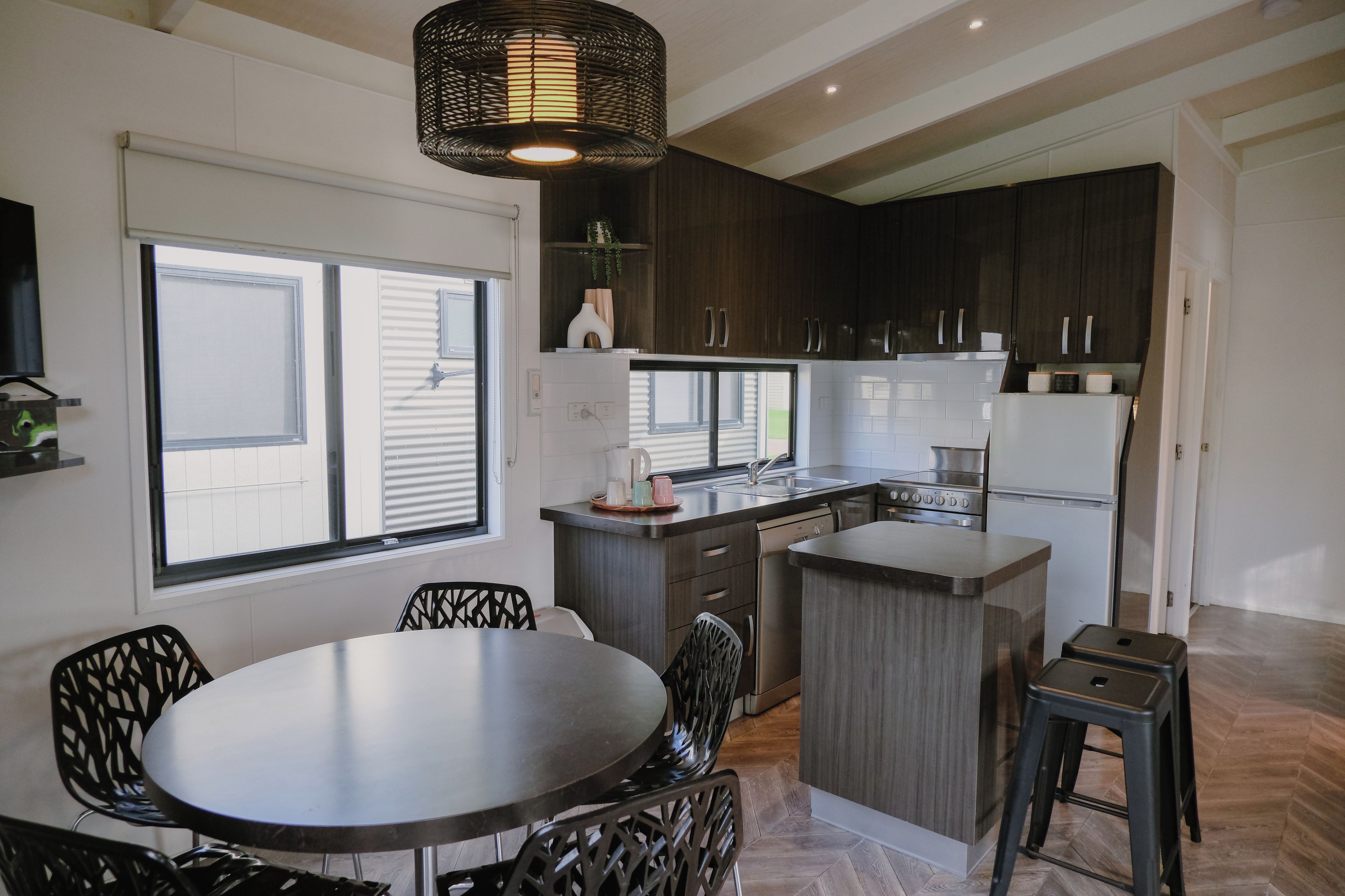 A modern kitchen with dark cabinetry, a round dining table, and a hanging light fixture.