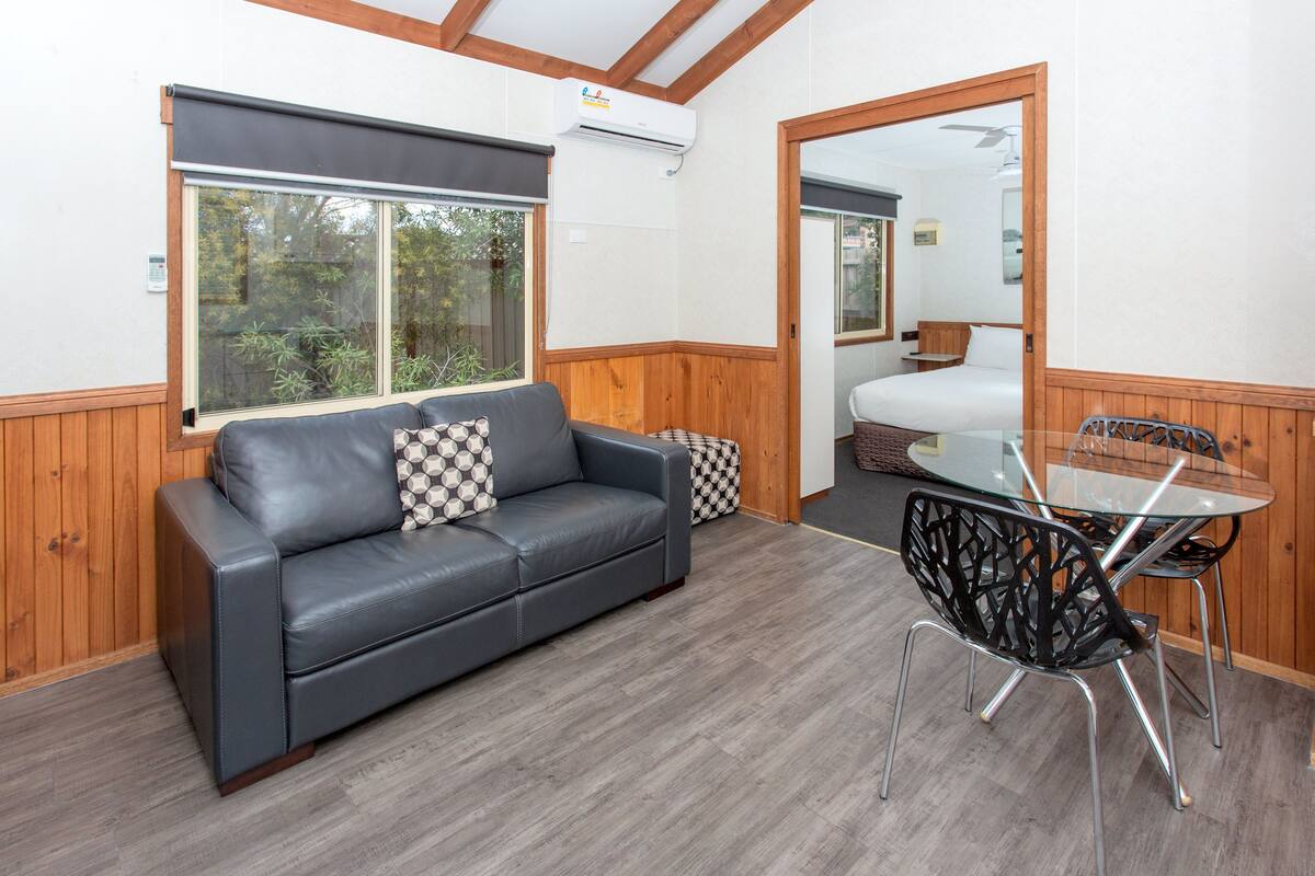 A room with a leather sofa, a glass table with metal chairs, and a wooden floor.