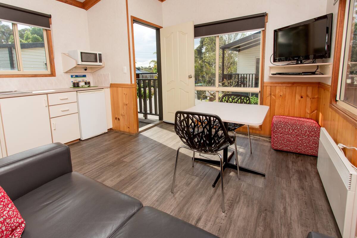 A compact living space with a kitchenette, a dining area with a table and chairs, a sofa, and a TV mounted on the wall.