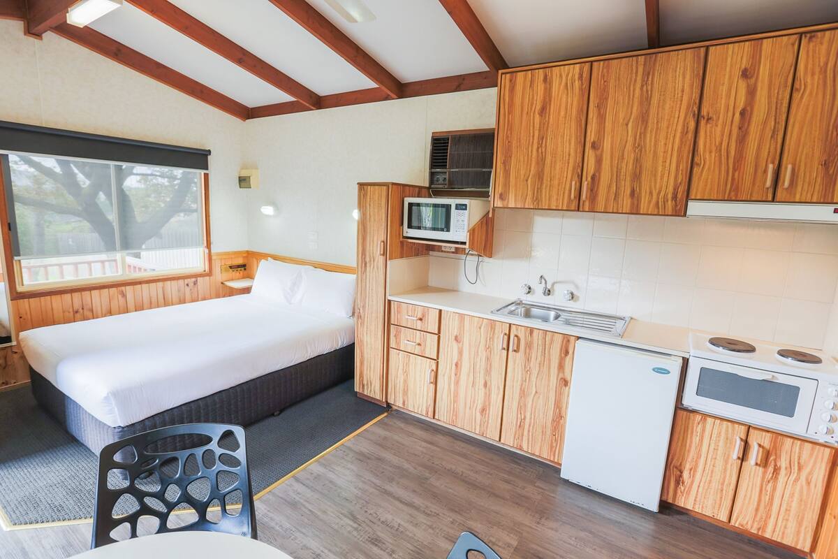 A compact room with a bed, kitchenette, and a window.