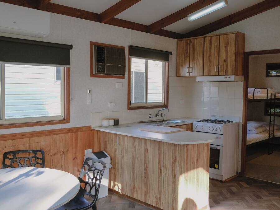 A compact kitchen with wooden cabinets, a central island, and a dining area with a table and chairs.