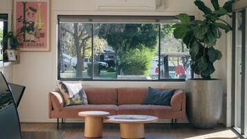 A modern interior with a sofa, two round coffee tables, a large potted plant, and a view of the outdoors through a window.